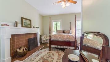 A bedroom with a four-poster bed, a fireplace, a mirror, and a ceiling fan.