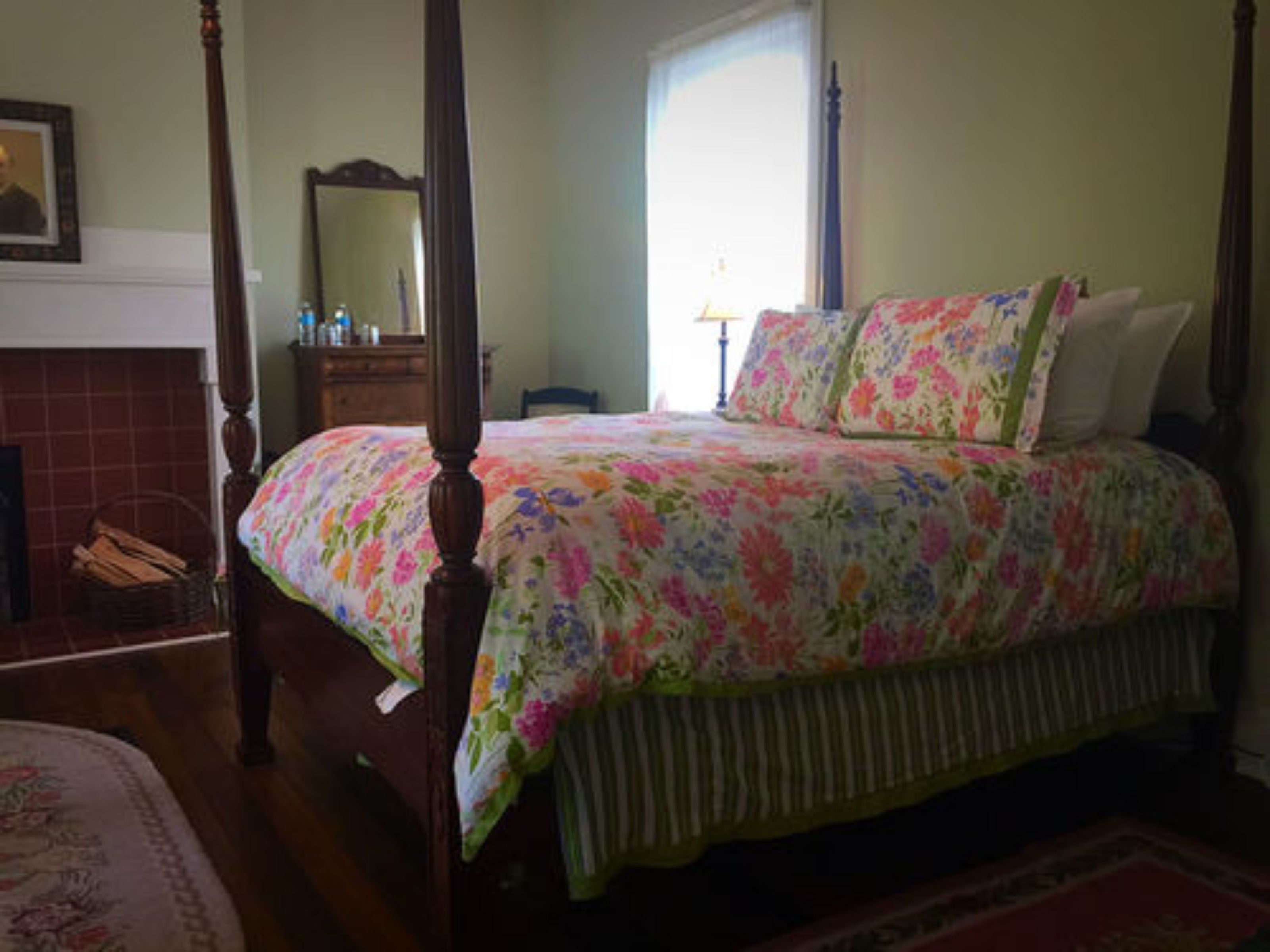 Un dormitorio con cama con dosel, cómoda, espejo y ventana con cortinas.