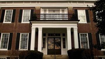 A two-story brick building with a central entrance flanked by columns, a balcony with decorative railings, and a number plaque.