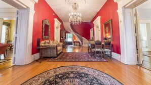 A spacious living room with a red accent wall, a chandelier, a staircase, and a dining area. - Bourbon Manor B&B (Bardstown)