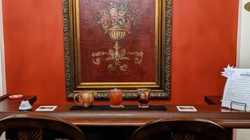 A bar area with a large sign reading "BAR" above a framed artwork. There are two wooden chairs in front of the bar, and a small table with a copper mug and two glasses on it.