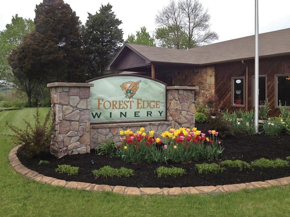 A sign for Forest Edge Winery with a stone border and a flower bed in front.
