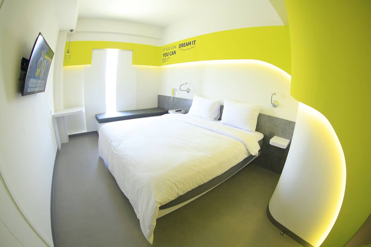 A modern hotel room with a large bed, a bedside table, a TV mounted on the wall, and a motivational quote on the wall.