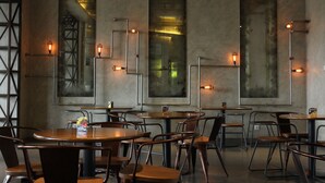 A restaurant with round tables and metal chairs, large windows, and pendant lighting.