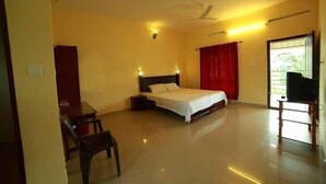 A bedroom with a bed, a chair, a television, and a window with curtains. - Kerala House (Peermade)