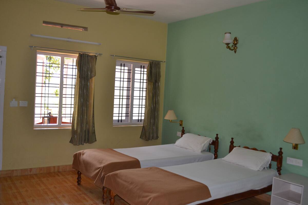 A room with two beds, a ceiling fan, and two windows with curtains.