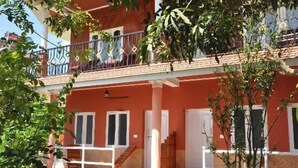 A two-story building with a red facade, white doors, and a balcony with a metal railing. - Kerala House (Peermade)