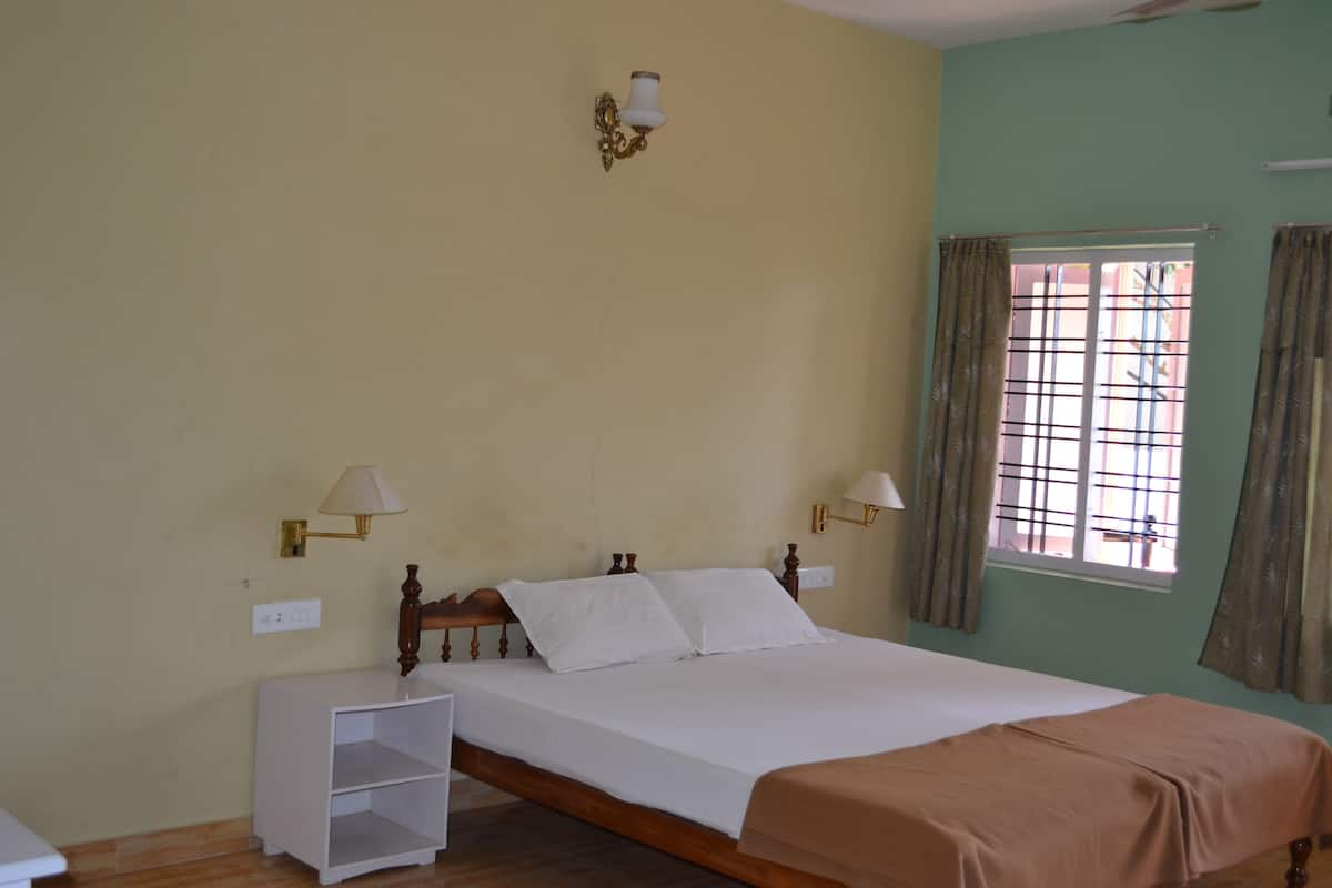 A bedroom with a wooden bed, two bedside lamps, a window with curtains, and a small white nightstand.