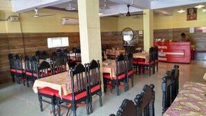 Ein Restaurant mit mehreren Tischen, Stühlen, einer Rezeption und Deckenventilatoren.