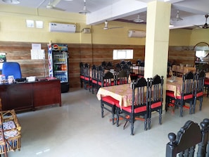 A dining area with tables and chairs, a refrigerator with beverages, and an air conditioning unit on the wall.