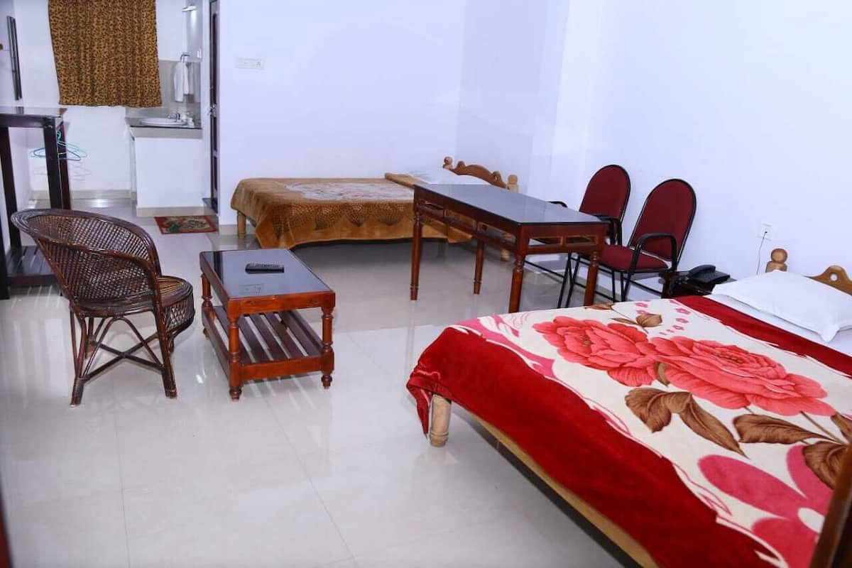 A hotel room with a bed, a wooden table, two chairs, a small stool, and a sofa.