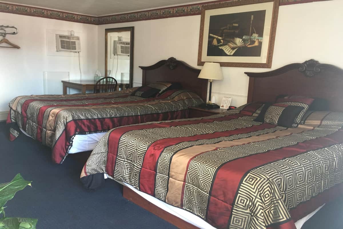 A hotel room with two beds, each with patterned bedding, a desk, and a chair.
