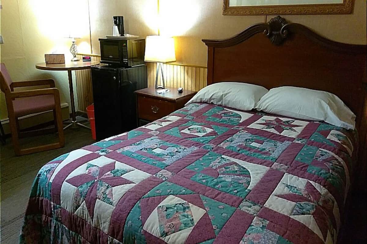 A bedroom with a bed, a chair, a desk with a computer, and a lamp.