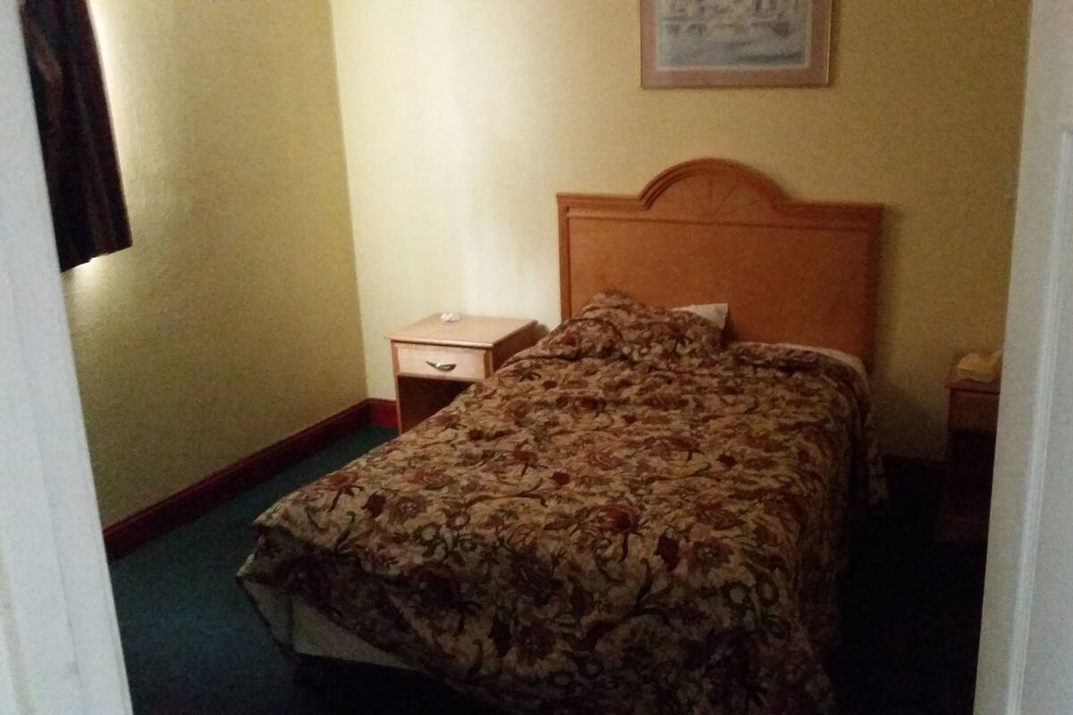 A hotel room with a bed, a nightstand, a small drawer, and a door.