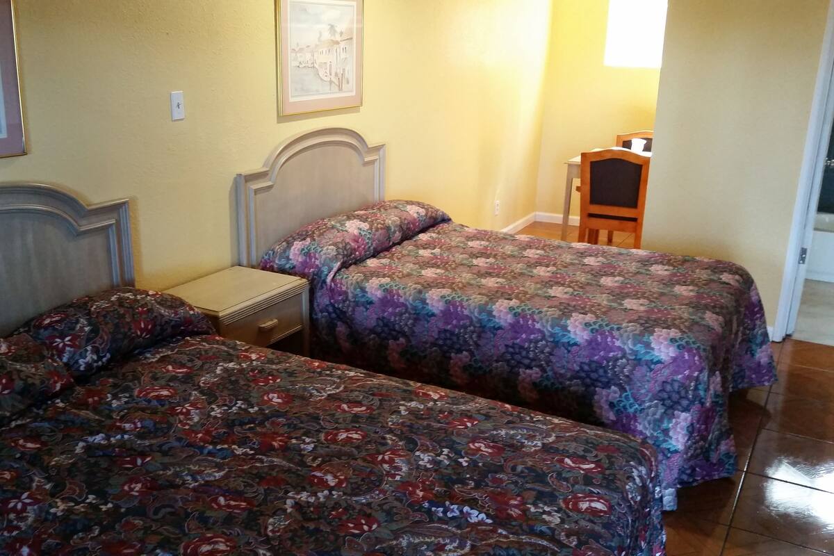 A room with two beds, each with floral-patterned bedding, a nightstand, and a framed picture on the wall.