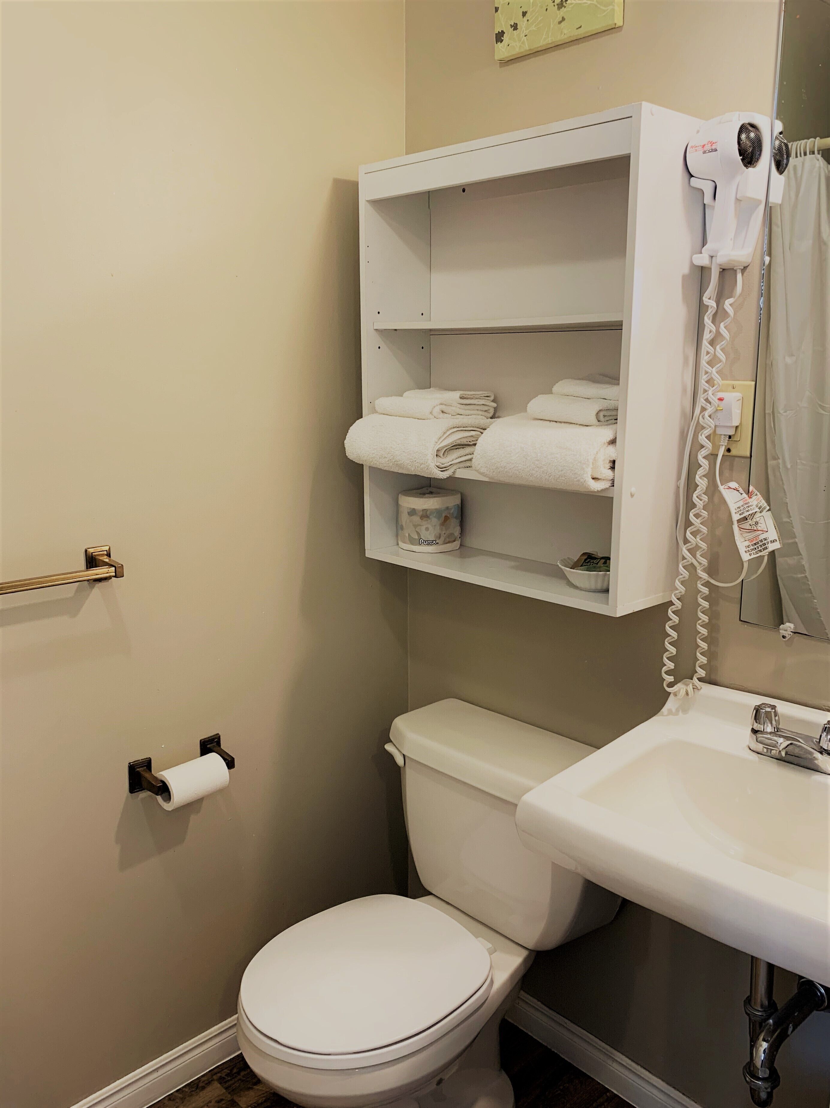 A small bathroom with a toilet, a sink, and a shelf with towels.