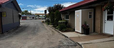 Un motel con un camino de grava, una gasolinera al fondo y un pequeño jardín con una planta en maceta.