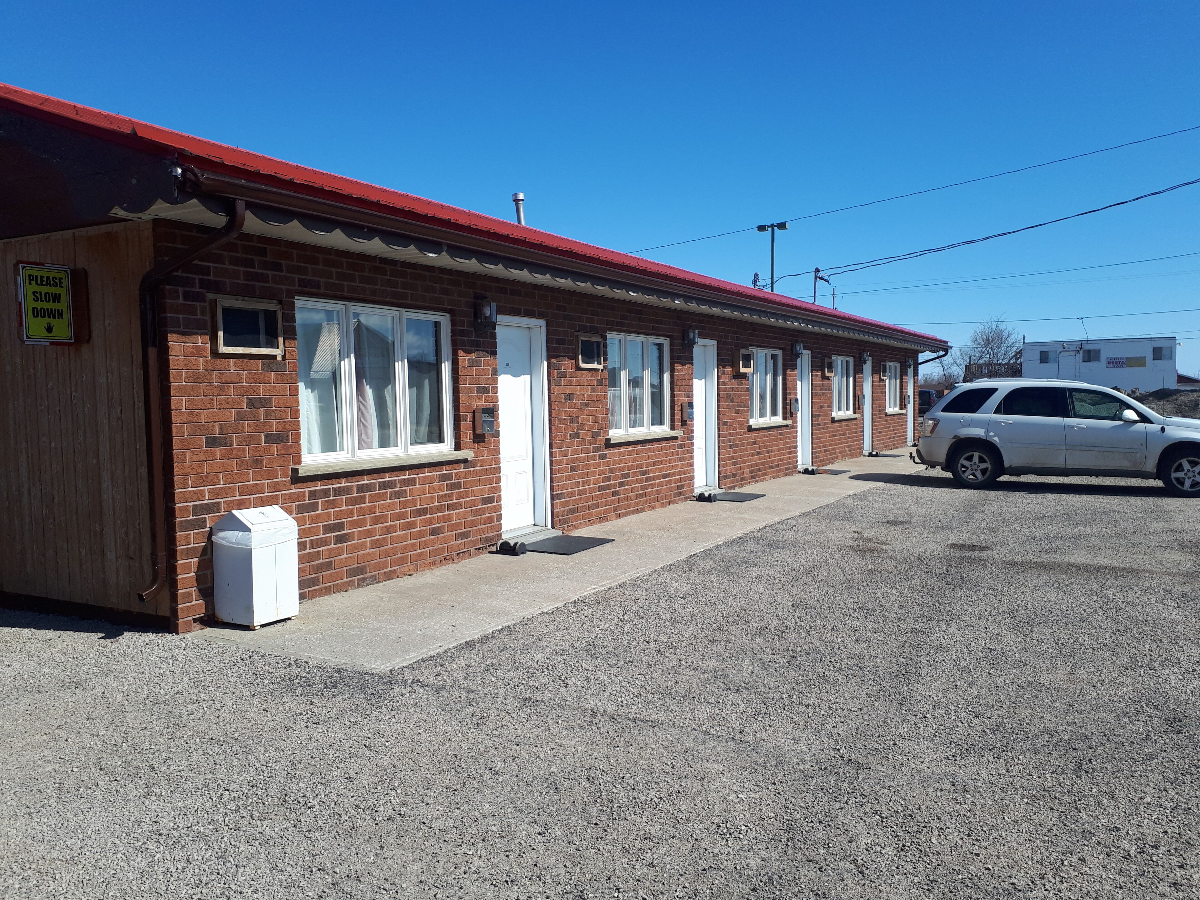 A motel with a red roof, brick exterior, and a gravel parking area.