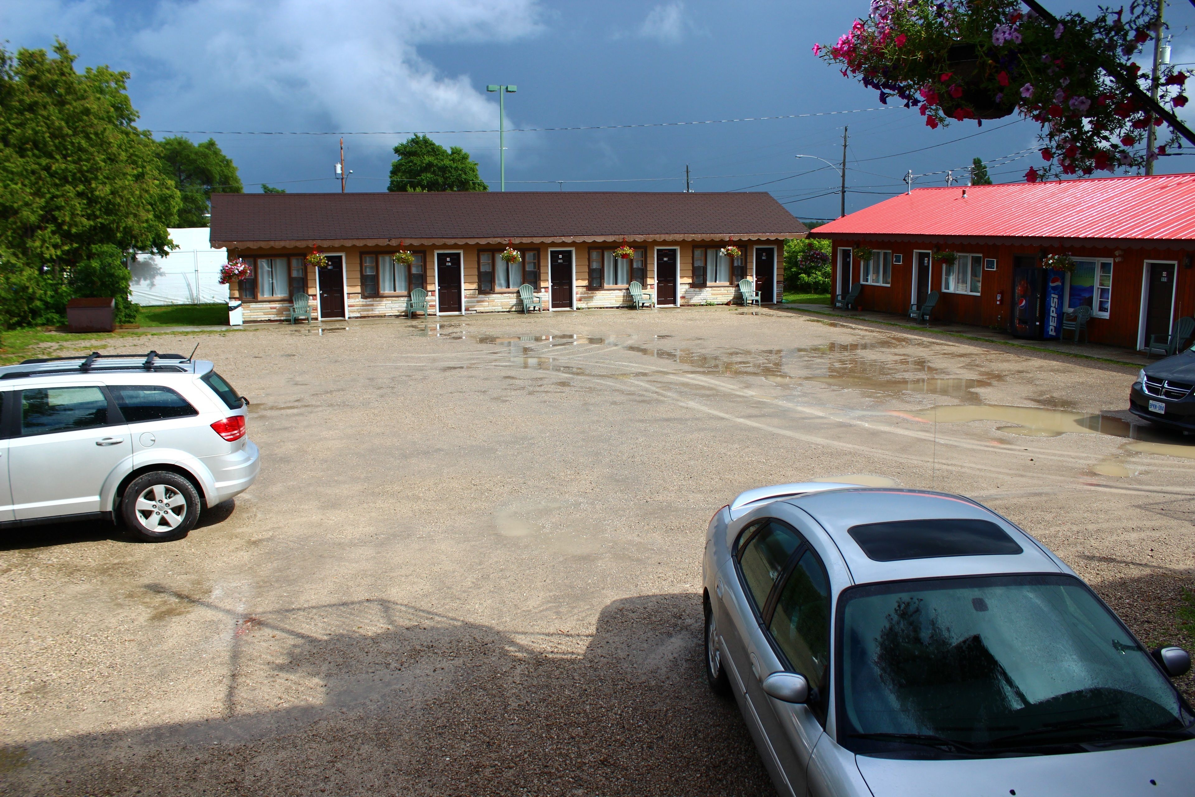 Un motel avec un toit rouge, plusieurs chambres et un parking.