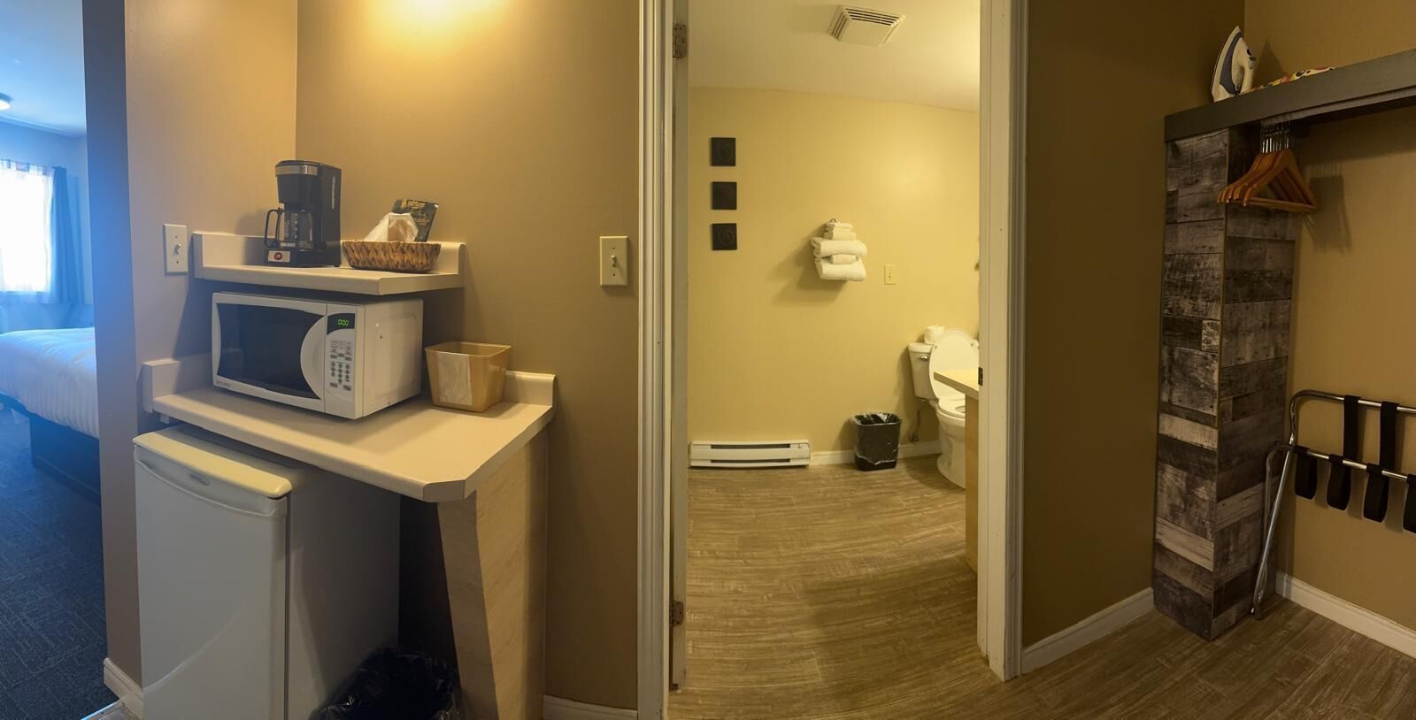 A hotel room with a kitchenette, a microwave, a small refrigerator, a trash bin, a heater, a toilet, and a shower area.
