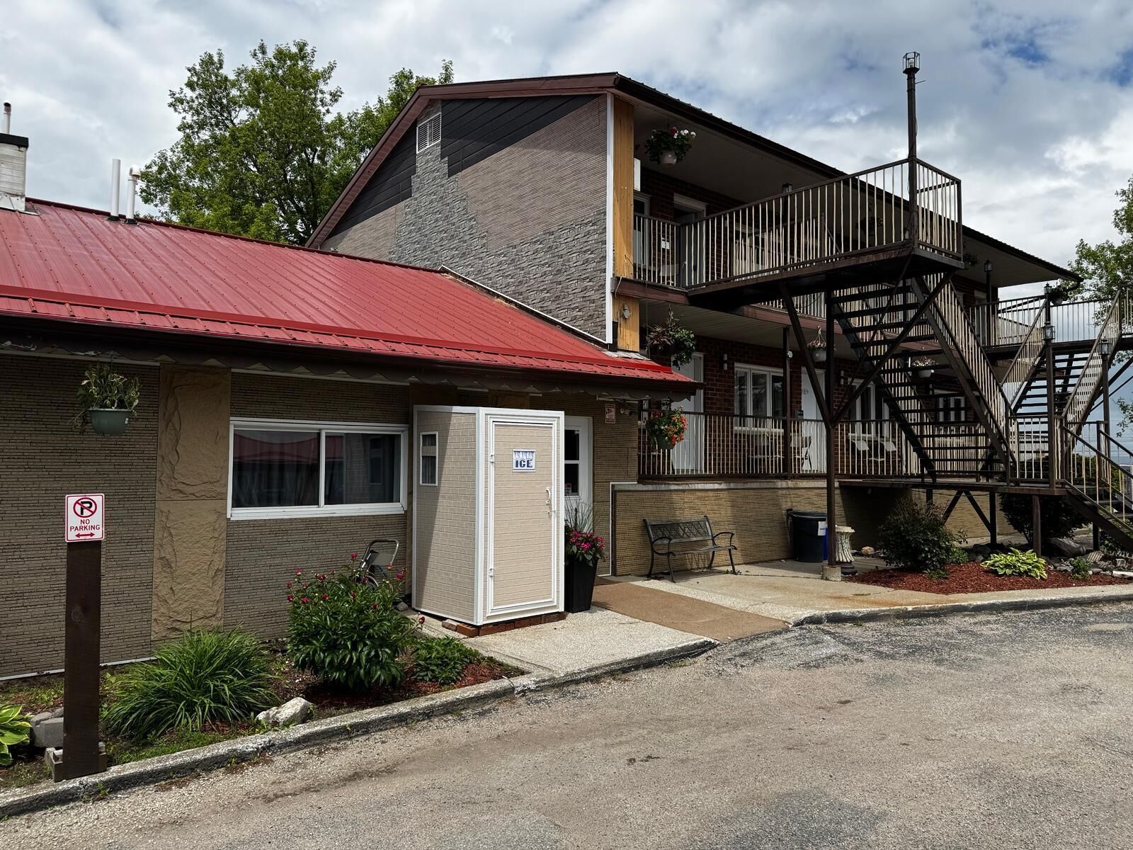 A two-story building with a red roof, a balcony with a metal railing, and a stairway to the upper level.