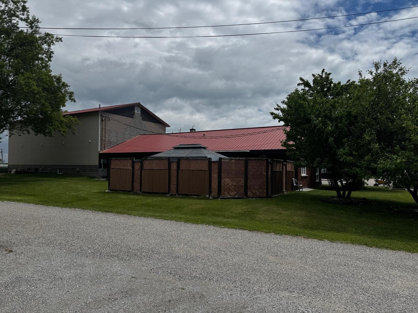 A building with a red roof, a covered outdoor area, and a gravel driveway.