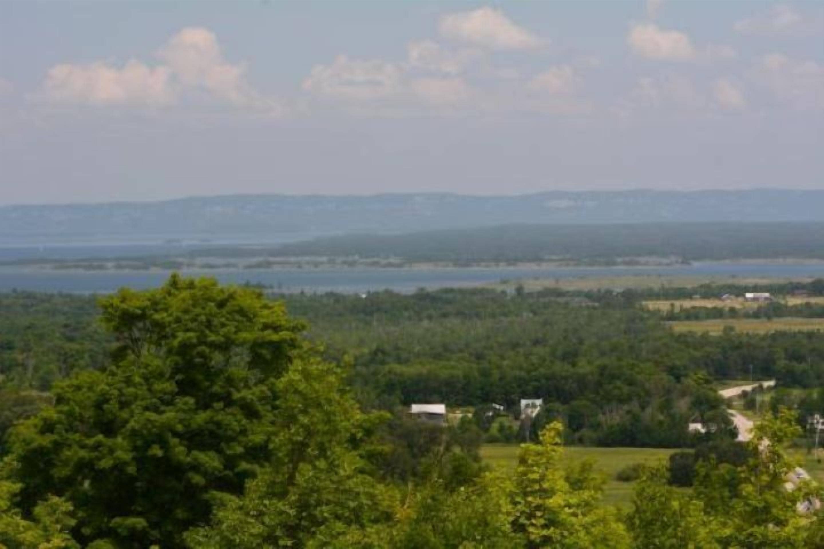 Eine Landschaft mit einem Gewässer, viel Grün und sanften Hügeln in der Ferne.
