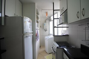 A compact kitchen with a refrigerator, washing machine, stove, and a small sink area. - Domingos 1101 (Rio de Janeiro)