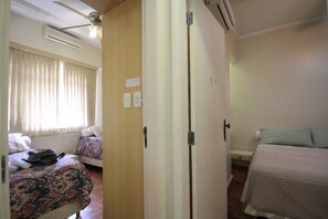 A hotel room with a bed, a bedside table, a chair, a window with blinds, an air conditioning unit, and a door. - Domingos 1101 (Rio de Janeiro)