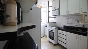 A compact kitchen with white cabinets, a black countertop, a stove, and a microwave.