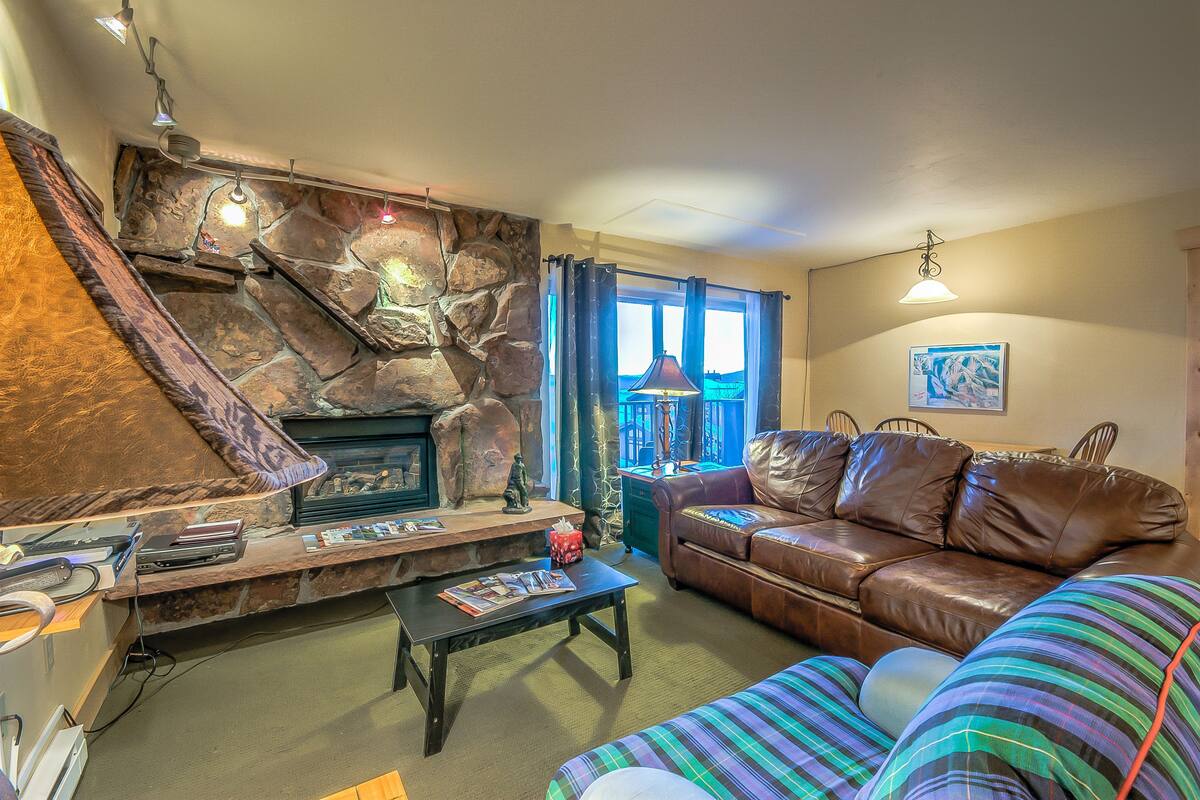A cozy living room with a stone fireplace, leather sofa, and a striped throw blanket.