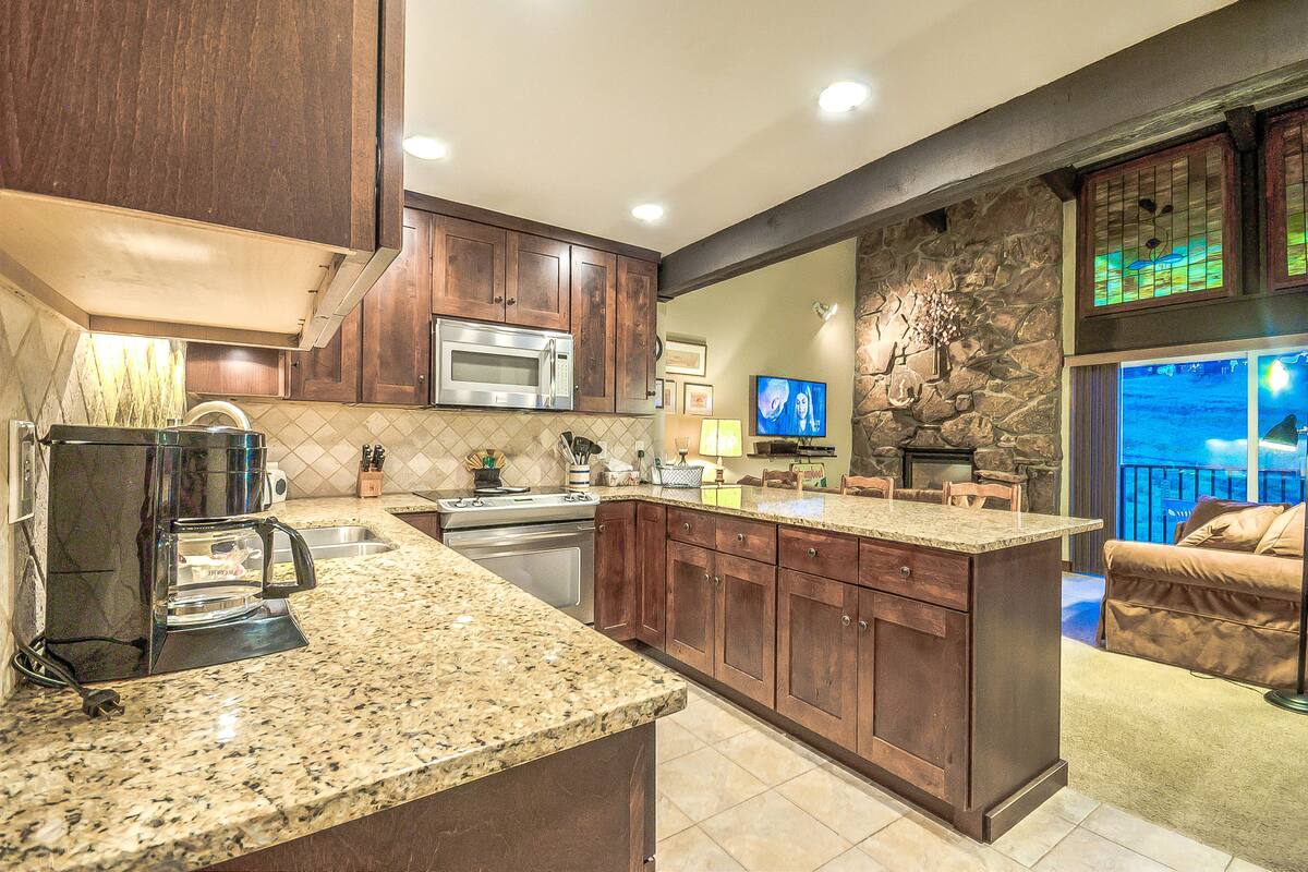 A kitchen with granite countertops, wooden cabinets, a built-in microwave, and a stone accent wall.