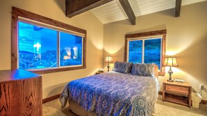 Une chambre à coucher avec un grand lit, deux tables de chevet et deux fenêtres équipées de lampes de chevet.