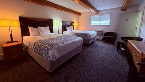 Une chambre d’hôtel avec deux lits, un bureau, une chaise et une fenêtre avec des stores.