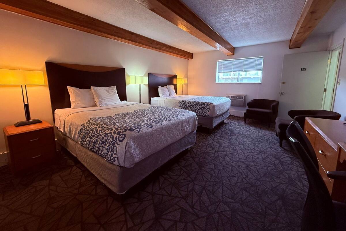 Een hotelkamer met twee bedden, een bureau, een stoel en een raam met jaloezieën.