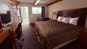 Une chambre d’hôtel avec un grand lit, un bureau avec un ordinateur, une télévision et une fenêtre donnant sur l’extérieur.