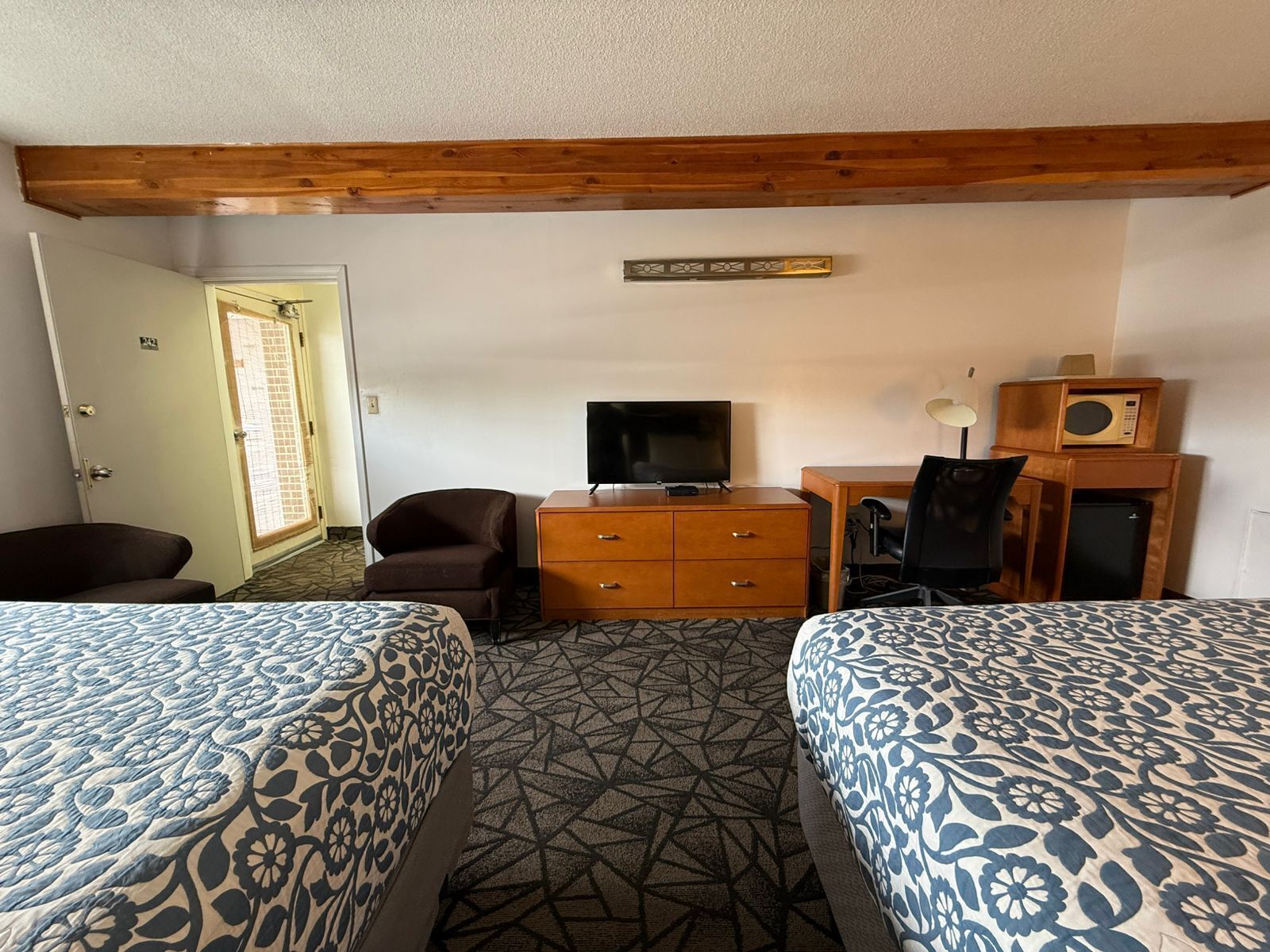 A hotel room with two beds, a TV, a desk with a computer, a chair, and a microwave.