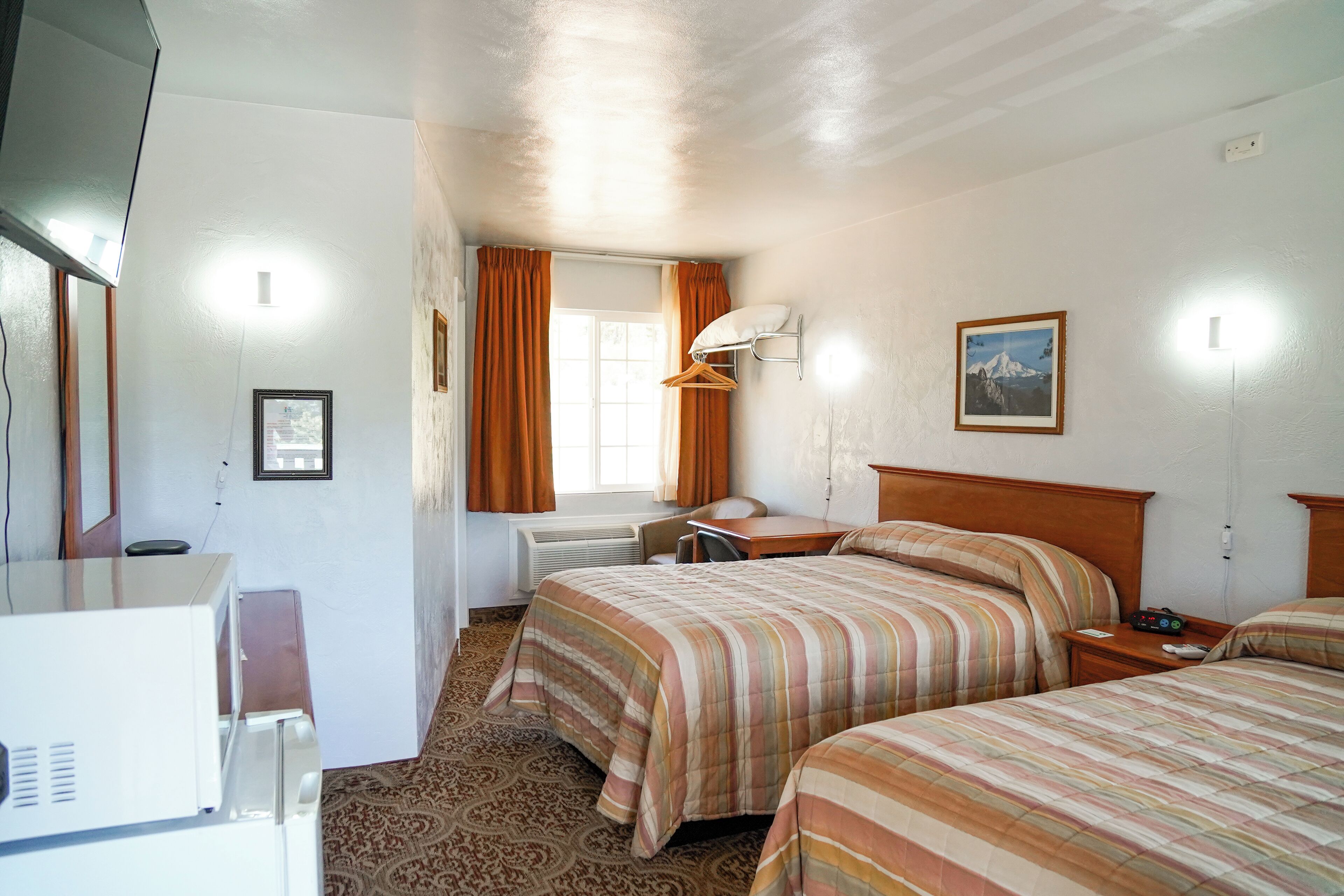 Une chambre d’hôtel avec deux lits, un bureau, une chaise, une lampe et un tableau au mur.