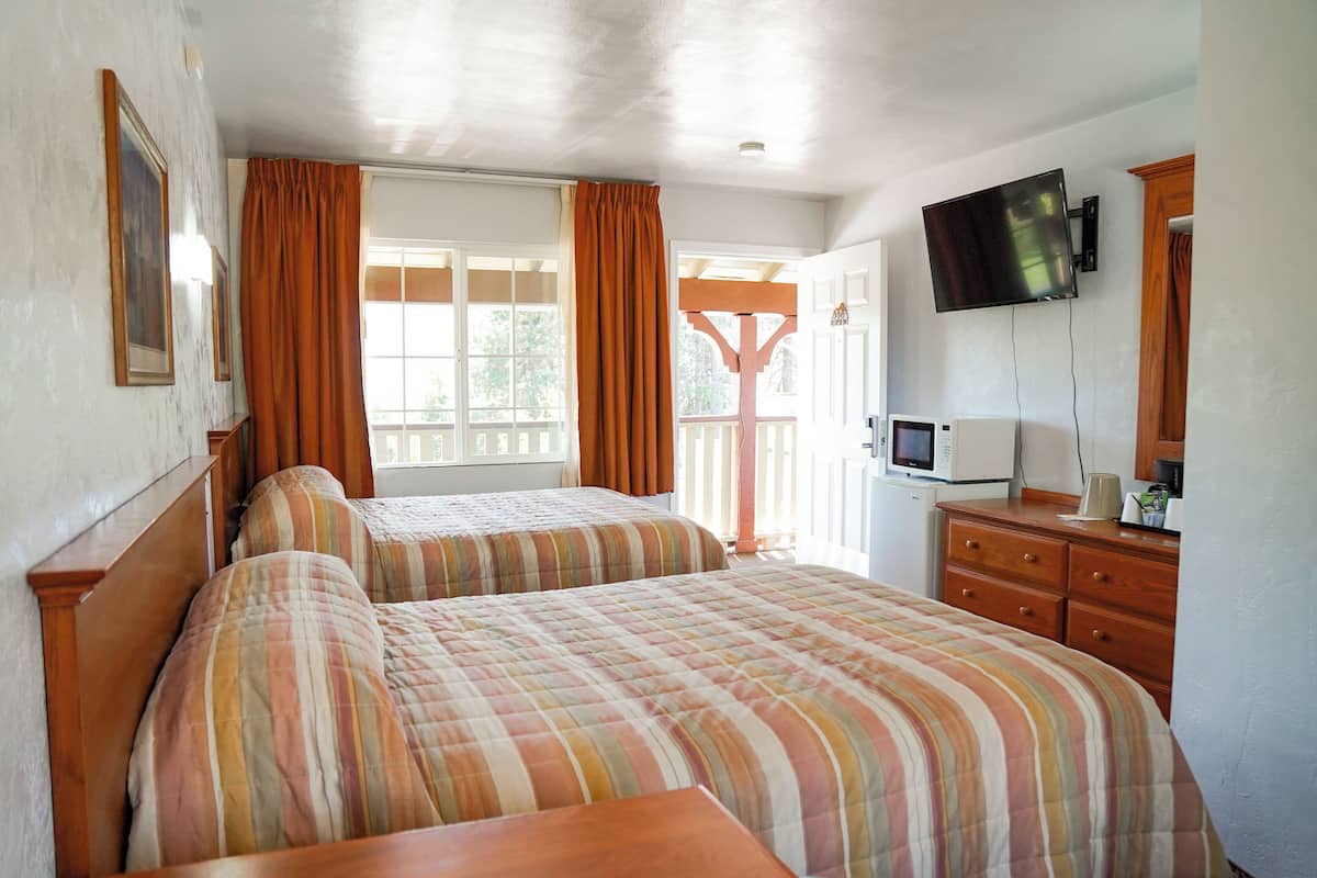 A room with two beds, a TV, a microwave, and a wooden dresser.