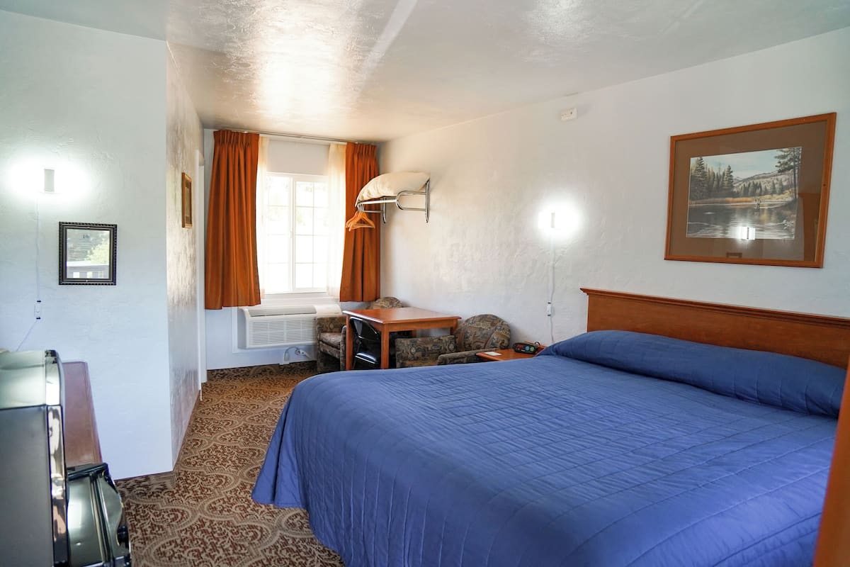 A hotel room with a bed, a desk, a chair, a window with curtains, and a framed picture on the wall.