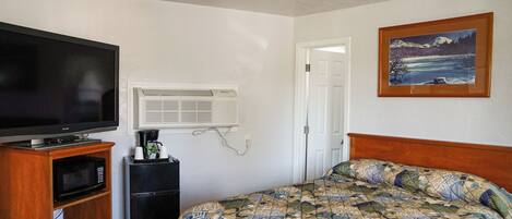 A hotel room with a bed, a television, a microwave, and a refrigerator.