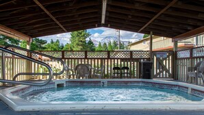 Un jacuzzi bajo una pérgola de madera con vistas a montañas.