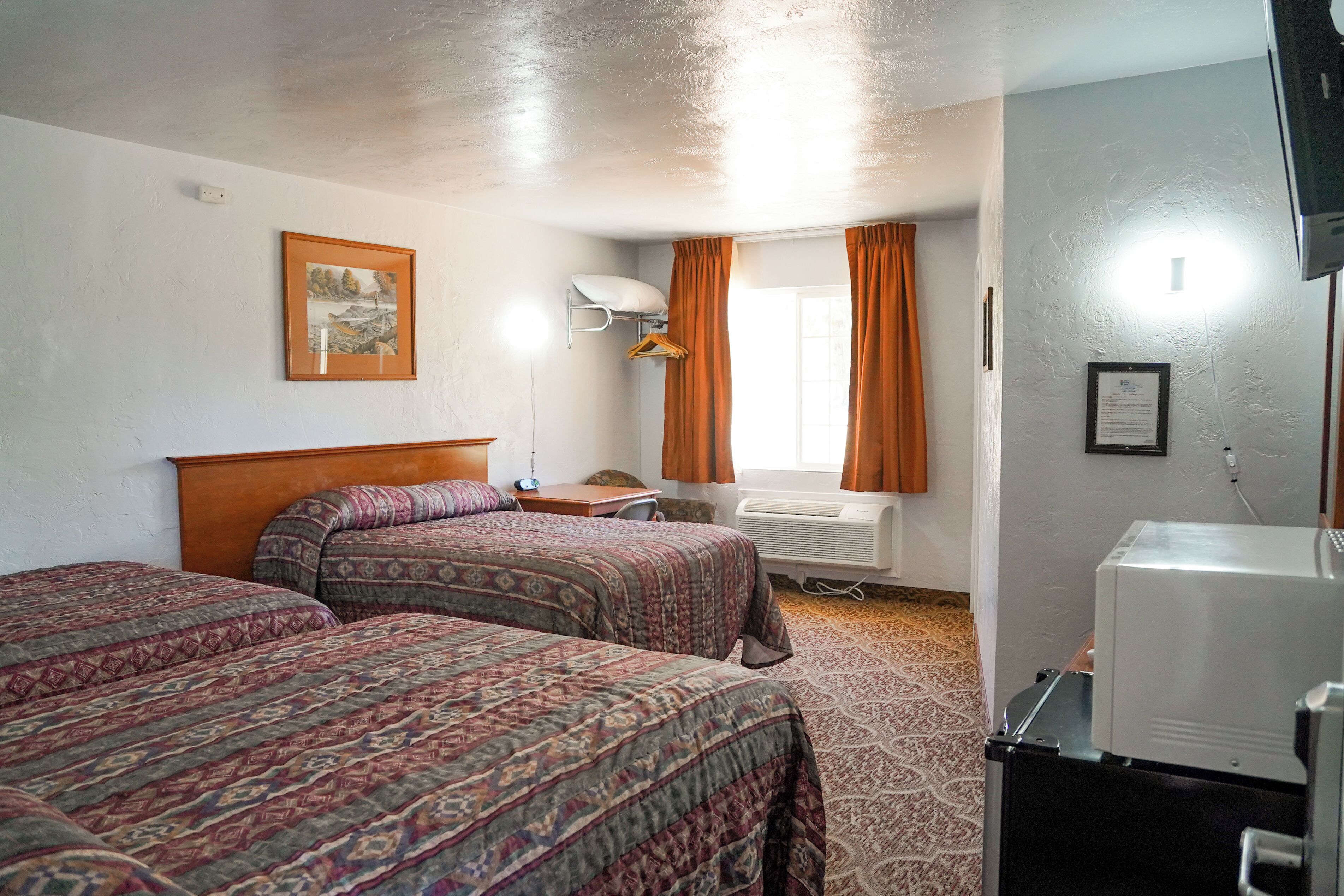 A hotel room with two beds, a desk, a chair, a heater, and a television.