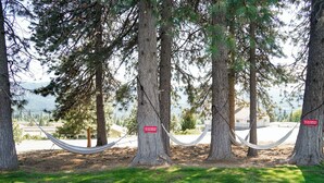 Una hamaca atada entre árboles en un área verde, con un letrero que dice 'Use the hammock at your own risk'.