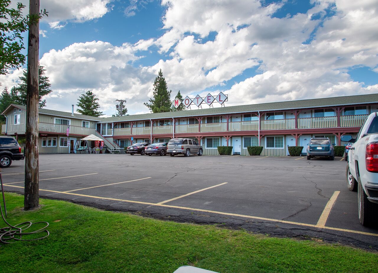 A motel with a parking lot, a row of rooms, and a sign indicating the motel name.