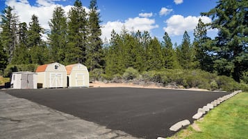 A paved parking area with two small buildings, one with a red roof and another with a white roof, surrounded by dense trees.