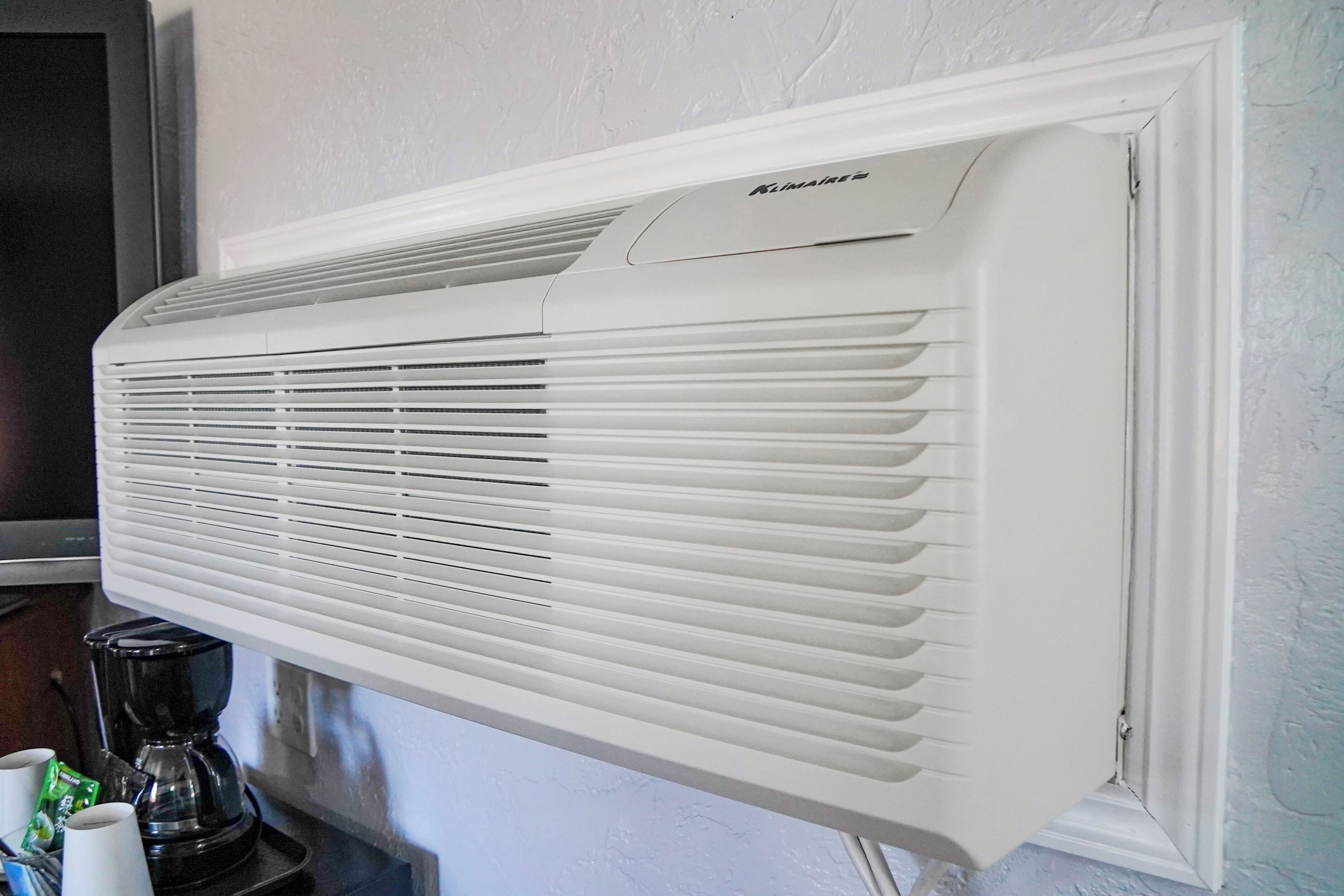 A white wall-mounted air conditioner with a control panel and a coffee maker on a table.