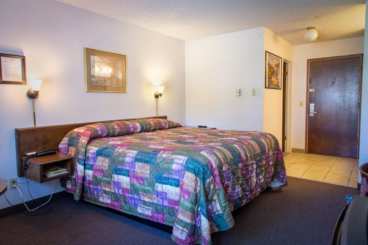 Quarto de hotel com uma cama grande, luminárias de cabeceira, um telefone e uma porta.
