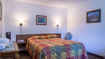 A hotel room with a large bed, two wall-mounted lamps, a bedside table with a lamp, a small table with towels, and a wall-mounted TV.