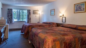 Habitación de hotel con dos camas, un escritorio, una silla, una ventana con cortinas e iluminación en la pared.